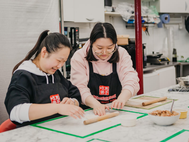 A teacher is rolling out dough with a cooking class student.